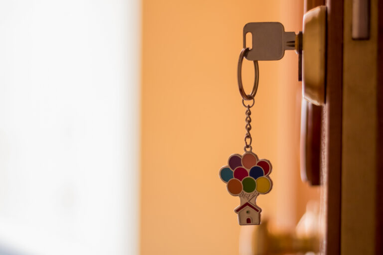 A key with a keychain of a house with colored balloons, on a wooden door with white and yellow background.